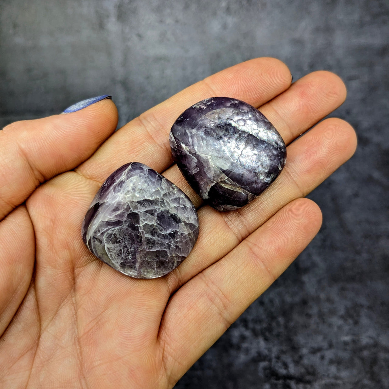 Hand holding two tumbled amethite stones from Gem Lepidolite 1.2’ Tumbled Stone #SK9941