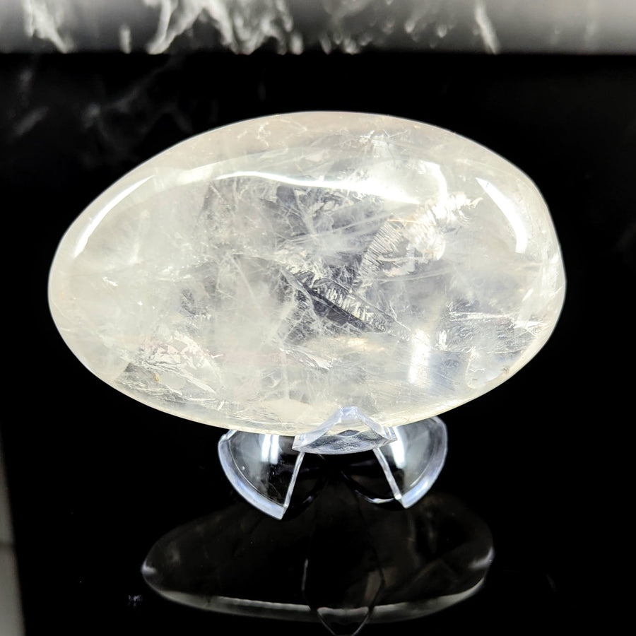 A translucent oval girasol quartz jumbo pebble with internal crystalline patterns on a clear acrylic stand