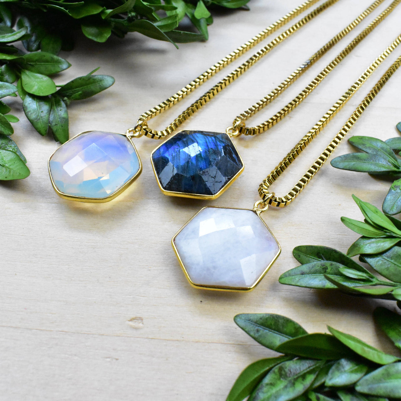 Three faceted hexagonal gemstone pendants on gold chains: moonstone, labradorite, quartz