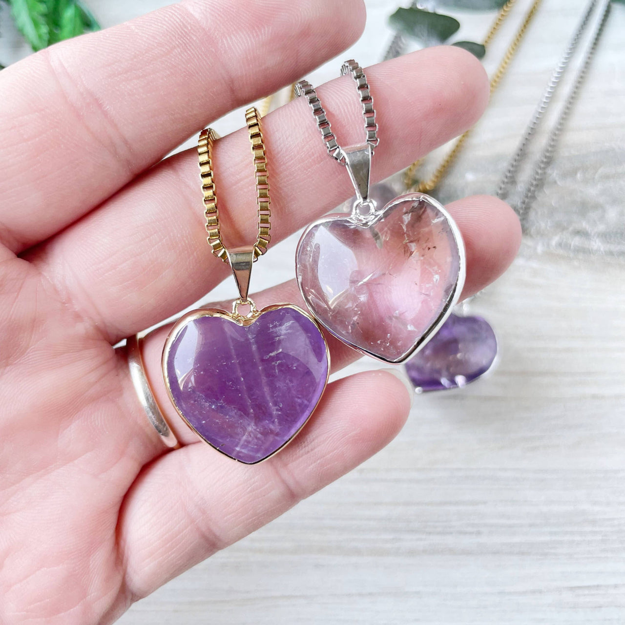 Hand holding gold amethyst and silver quartz heart necklaces LV9397