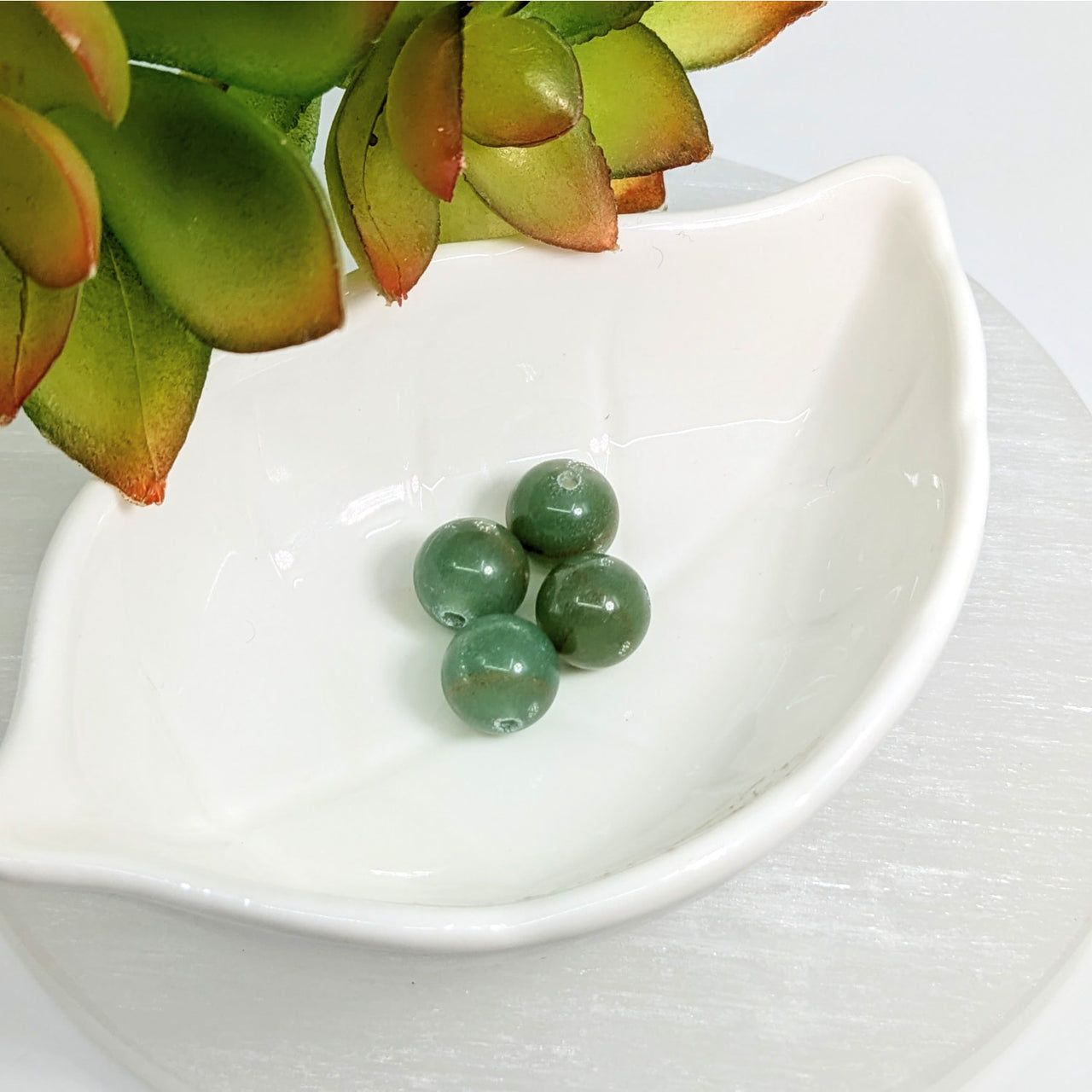 Four green aventurine 10mm round beads in a white ceramic dish for crafting