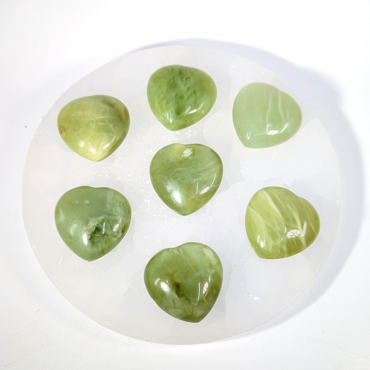 Seven polished 1.1-inch green jade mini heart stones in circle on white plate