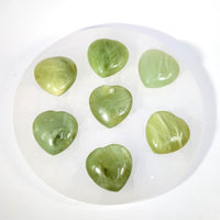 Seven polished 1.1-inch green jade mini heart stones in circle on white plate