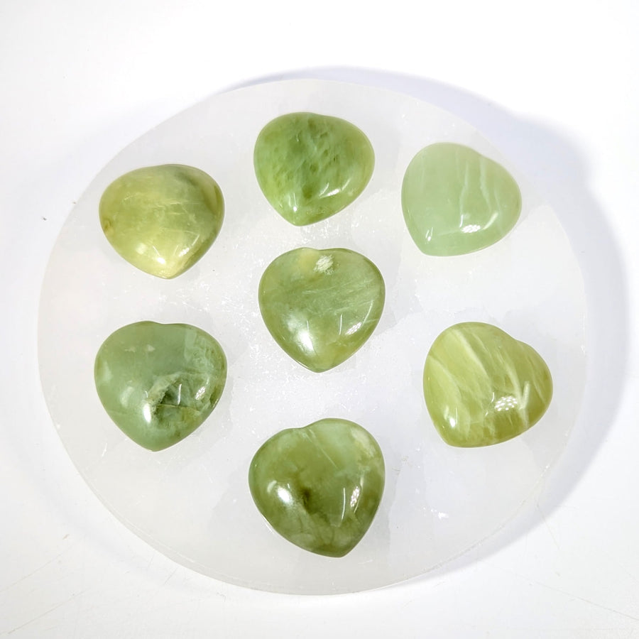 Seven polished 1.1-inch green jade mini heart stones in circle on white plate