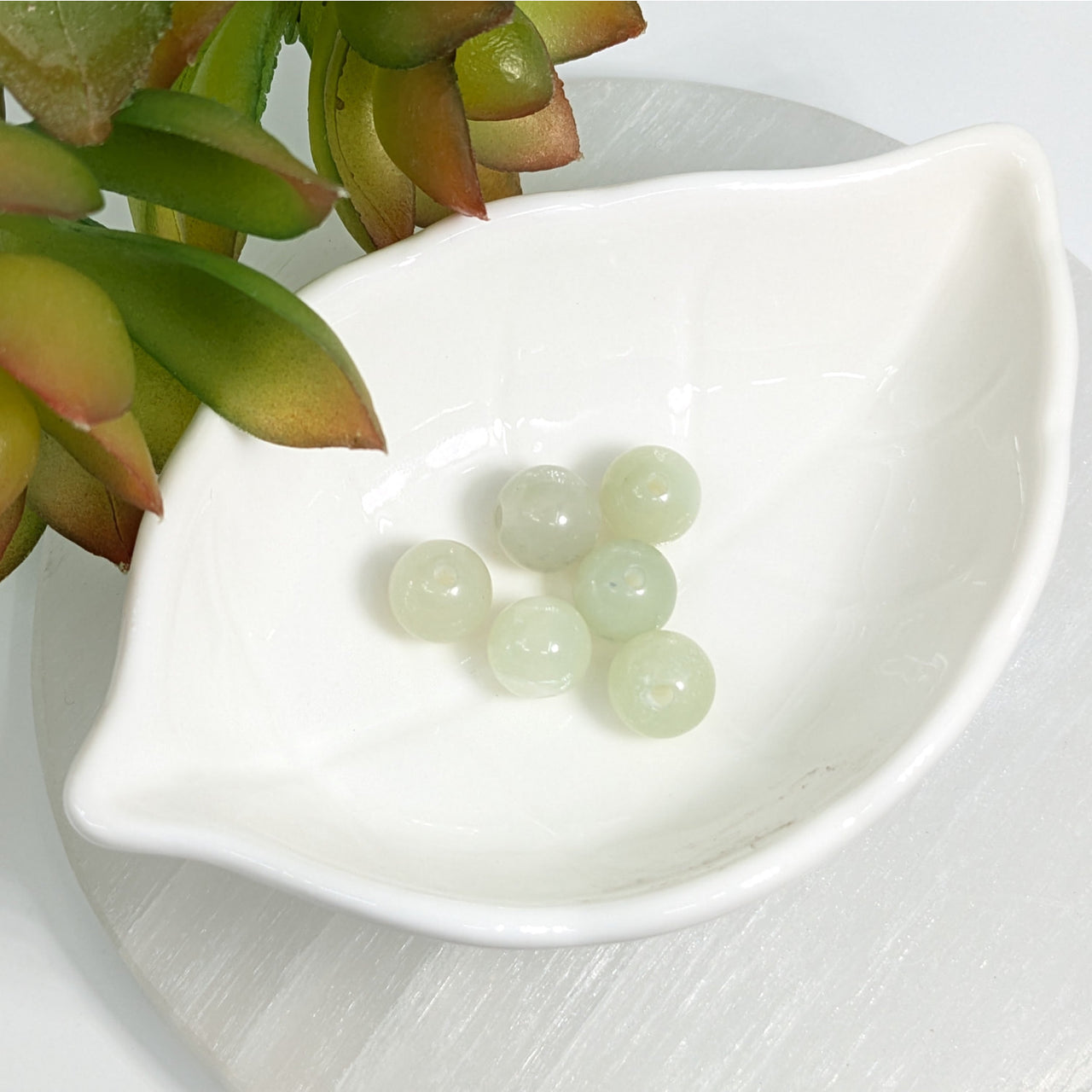 White ceramic dish with green jade 10mm round beads showcasing natural beauty