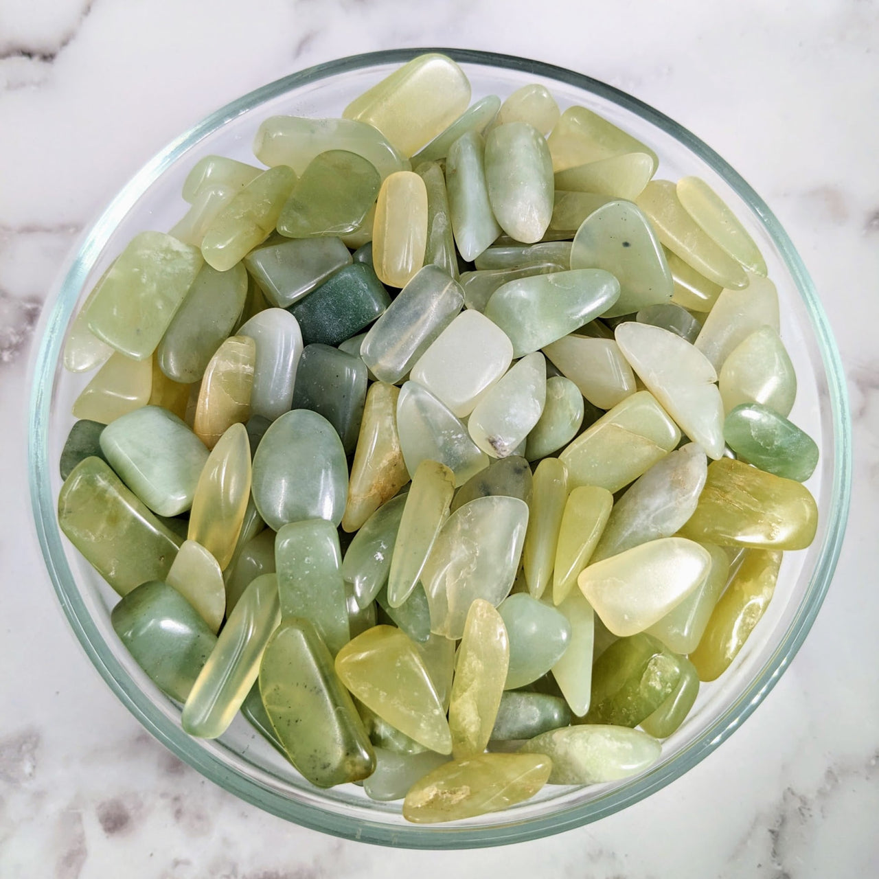 A bowl filled with green and yellow tumbled stones, perfect for collectors