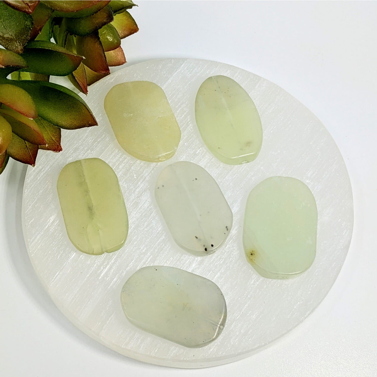 Six pale green jade 37mm organic oval beads arranged on a white plate