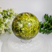 Green opal 2.7 inch polished sphere with golden flecks and dark inclusions on clear acrylic stand
