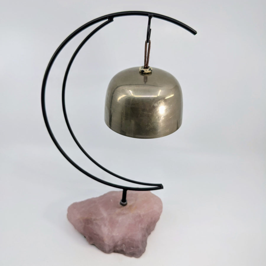 Metal bell hanging on a crescent moon stand with rose quartz base for healing and meditation