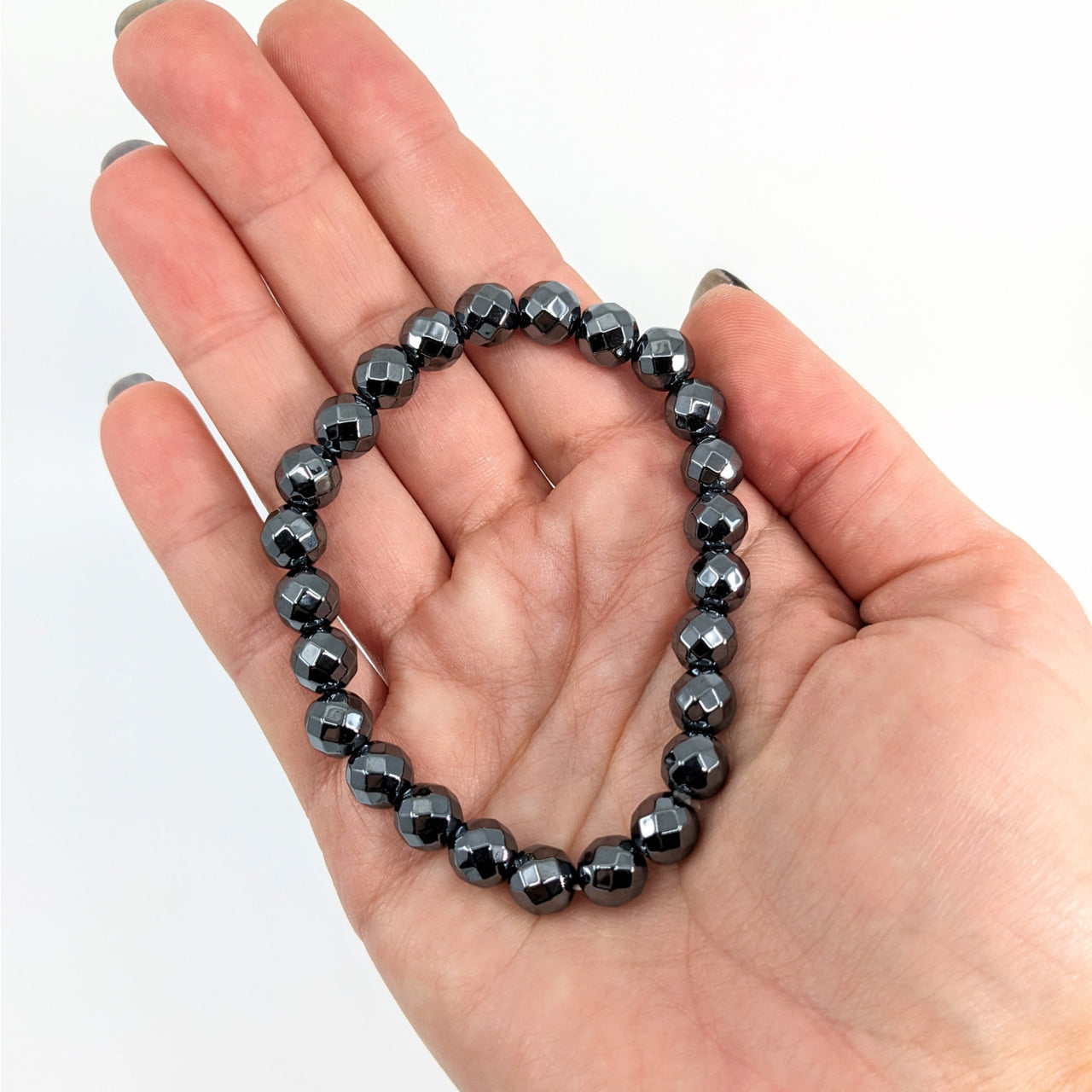 Hand holding Hematite Bracelet, Style #J258, showcasing its sleek black and white design