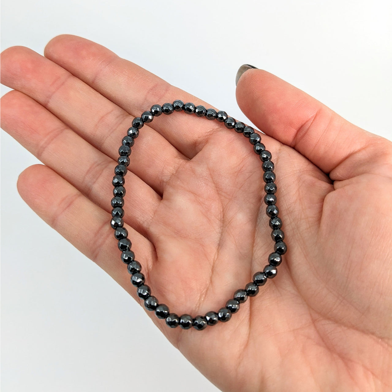 A hand holding a black beaded Hematite Bracelet, Style #J258 - perfect for any outfit