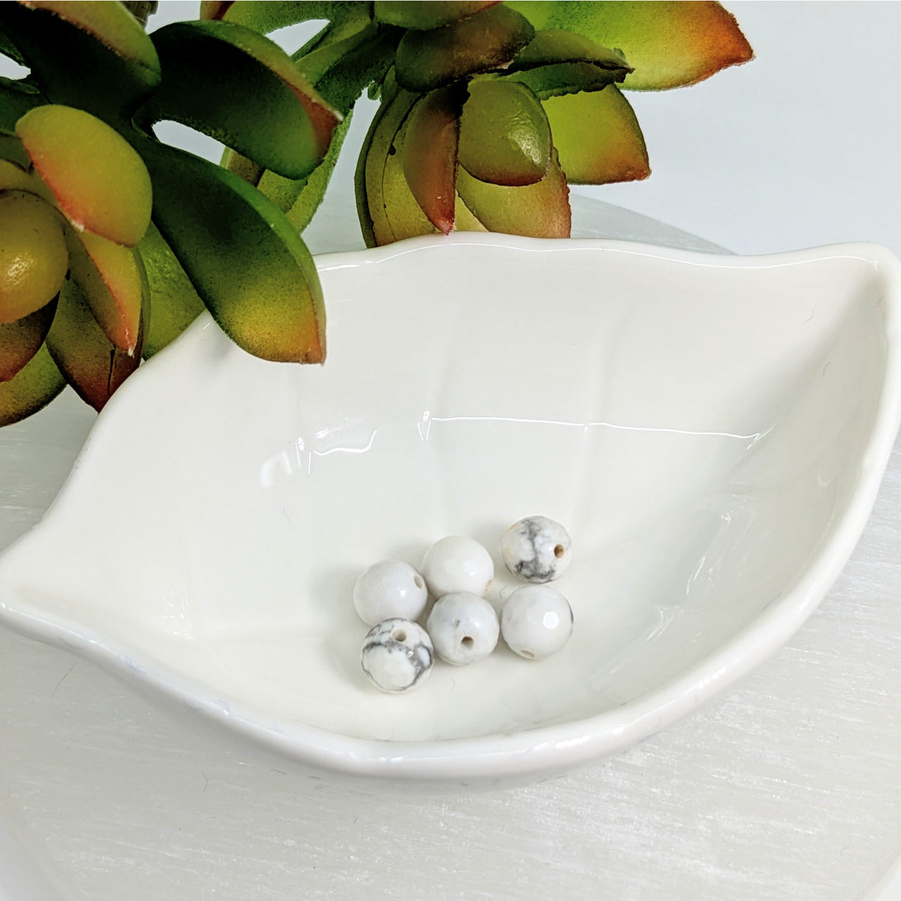 White ceramic leaf-shaped dish displaying Howlite 7.5mm round faceted beads pack