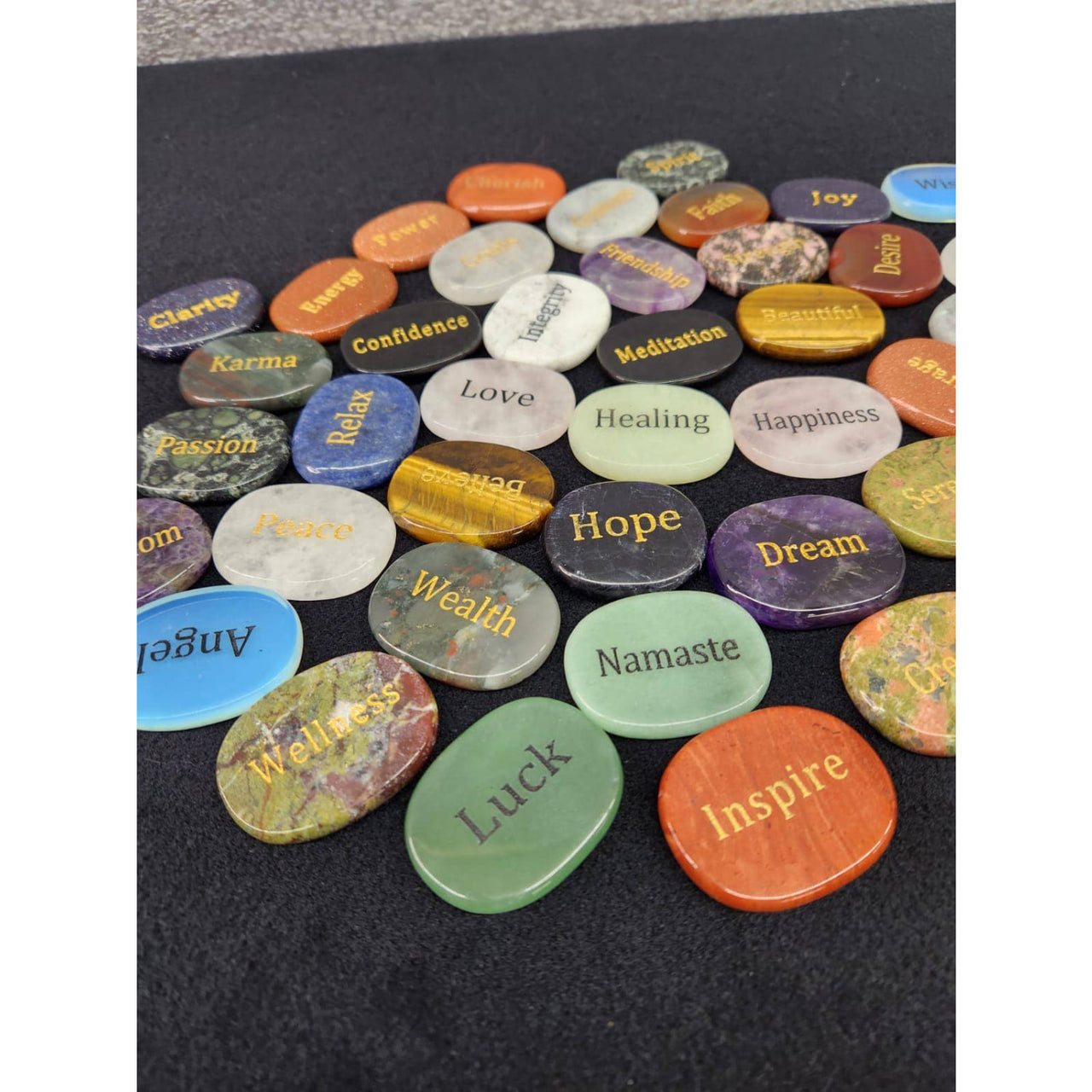 Multicolored crystal affirmation palm stones with engraved words on dark surface