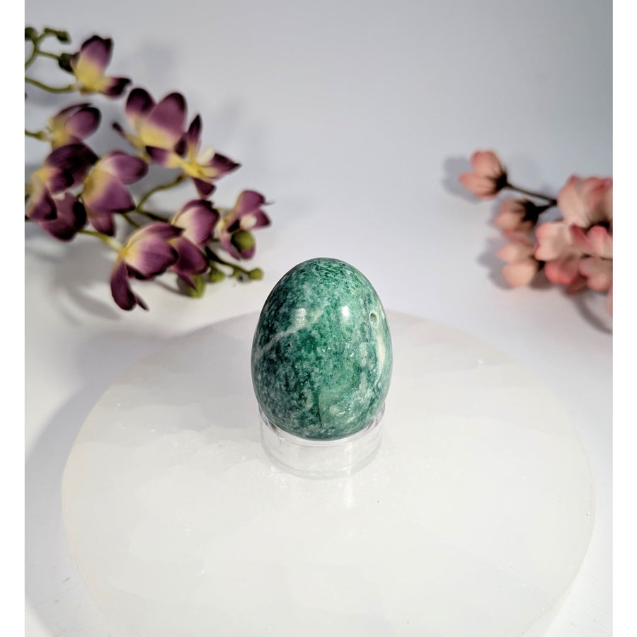Smooth oval green jade yoni egg with hole and white veining on acrylic stand