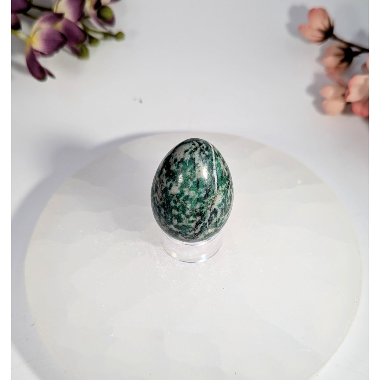 Polished green and white speckled jade yoni egg with hole on acrylic stand