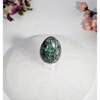 Polished green and white speckled jade yoni egg with hole on acrylic stand
