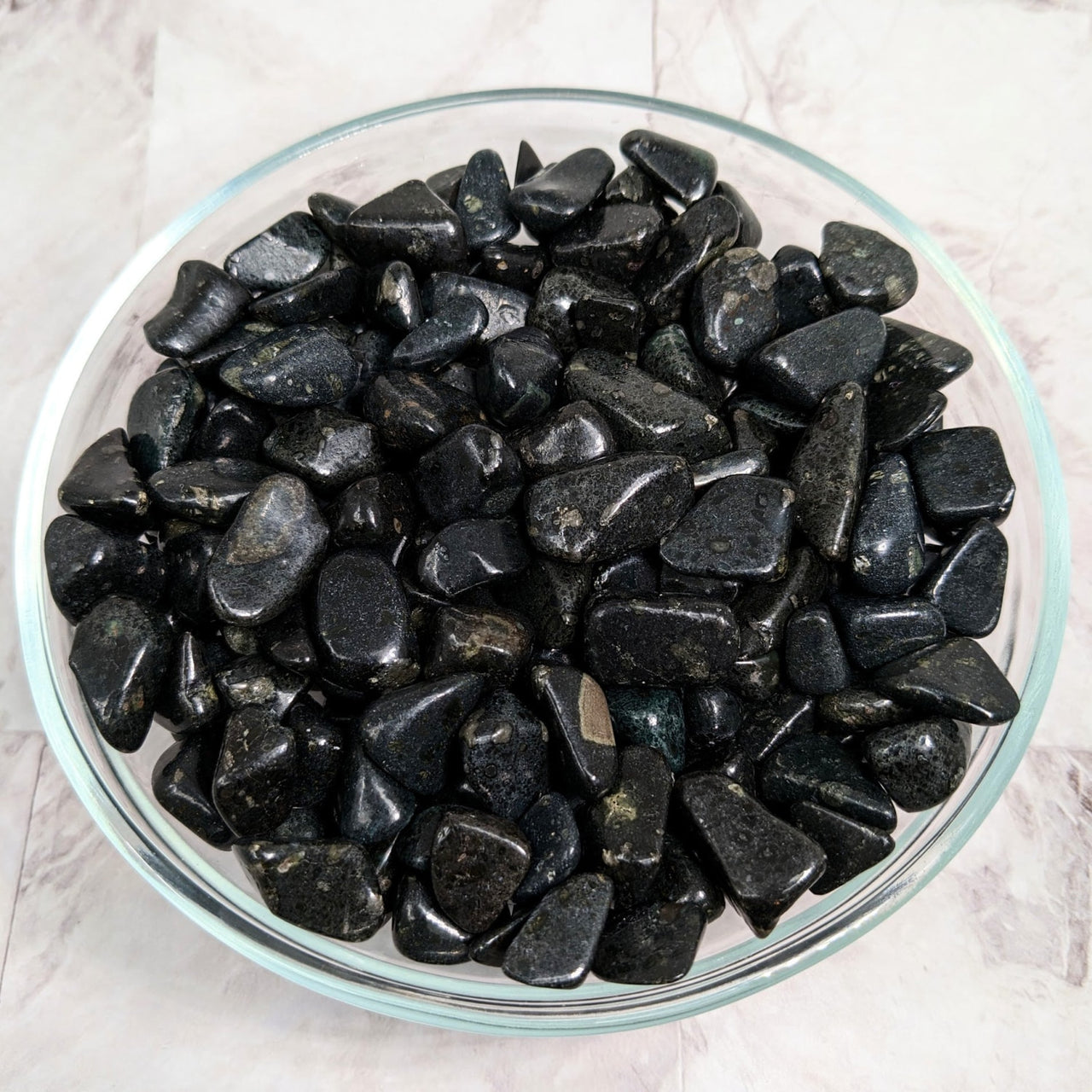 A bowl of tumbled black stones from South Africa on a marble counter