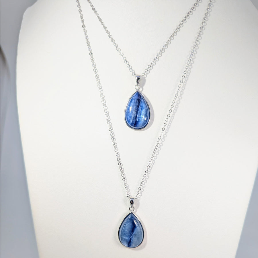 Two silver necklaces with blue teardrop Kyanite pendants on a white background