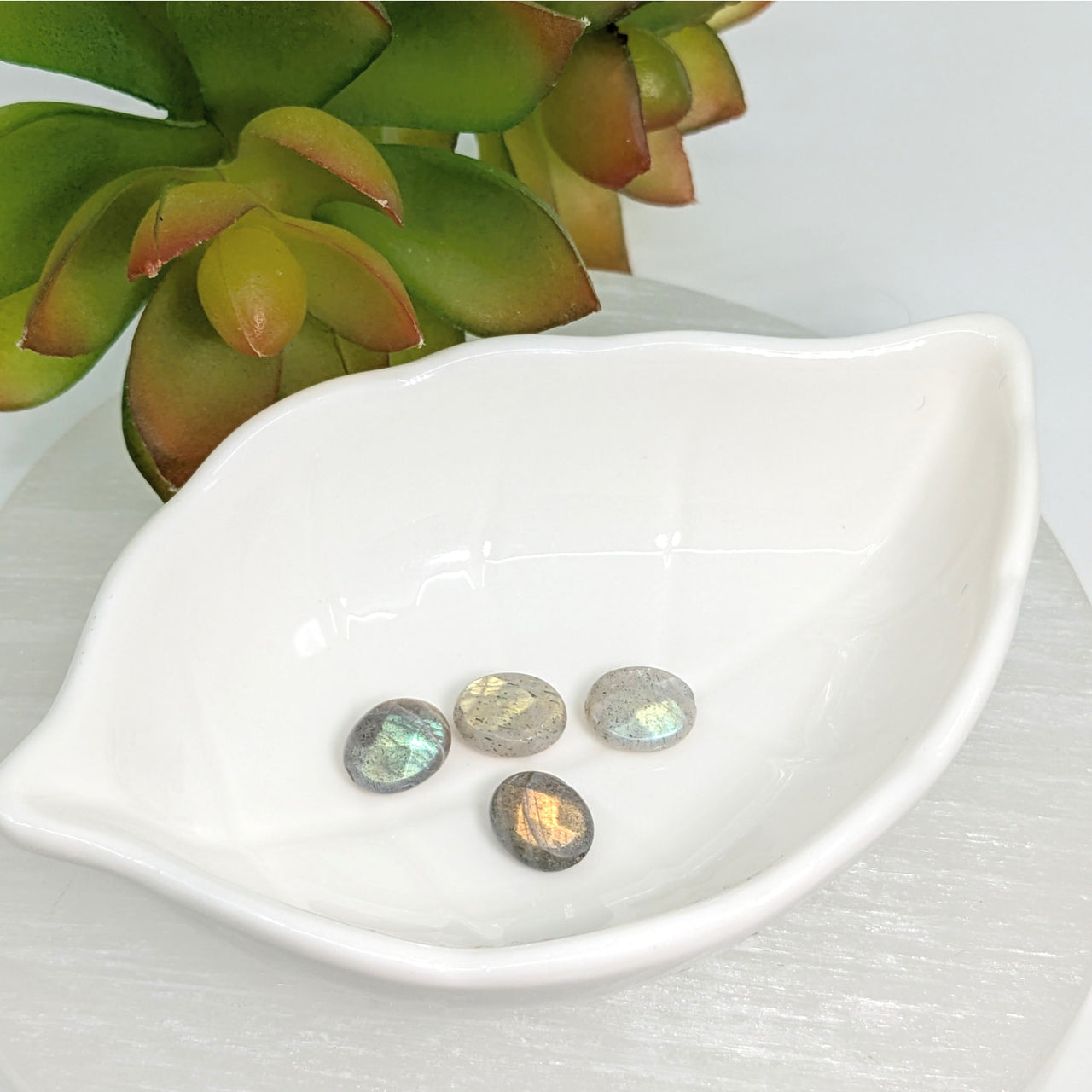 White leaf-shaped dish with four iridescent Labradorite 11mm Faceted Oval Beads