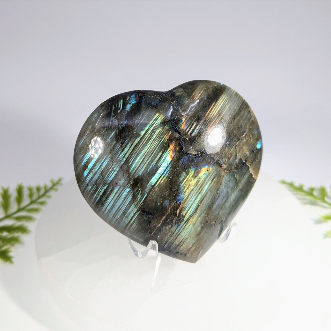 A polished 3 inch heart-shaped labradorite gemstone with shimmering blue and green hues perfect for jewelry and crystals