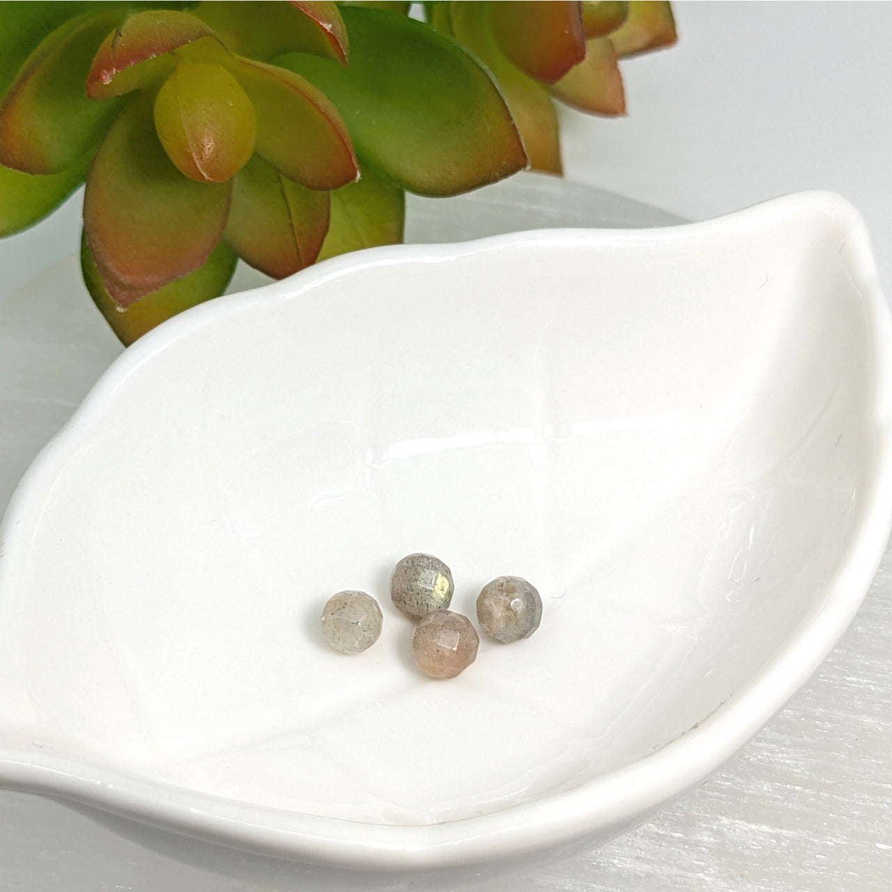 White leaf-shaped ceramic dish with Labradorite 6mm faceted round beads displayed