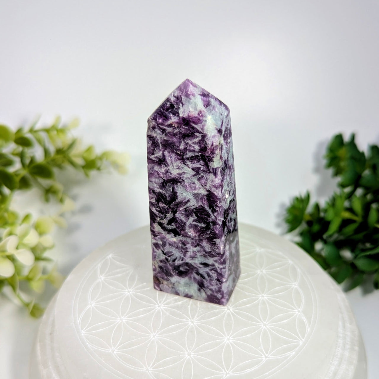 A polished purple and white fluorite crystal tower with a pointed top standing upright on a white circular base
