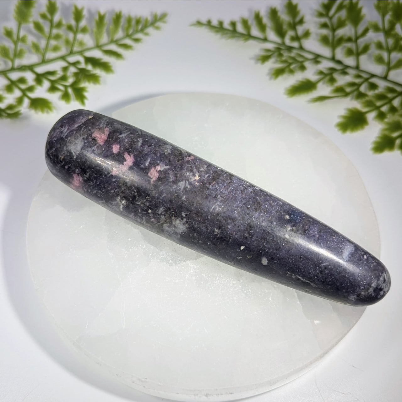 A polished dark purple lepidolite crystal massage wand with pink speckles and smooth elongated oval shape for healing