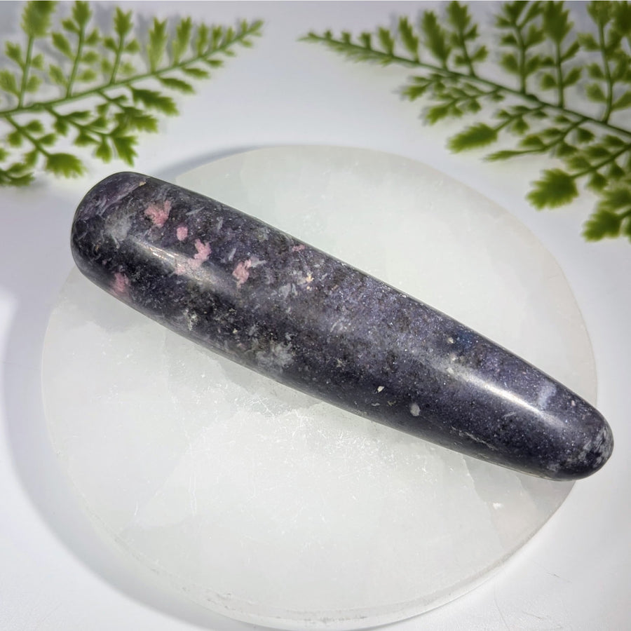 A polished dark purple lepidolite crystal massage wand with pink speckles and smooth elongated oval shape for healing