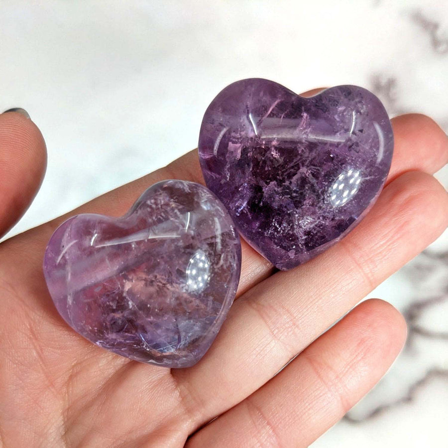 Two Lilac Amethyst drilled heart pendants in a person’s palm