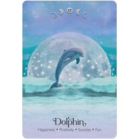 A dolphin leaps in front of a large sparkling moon on the lunar magic oracle deck with teal and purple ocean colors