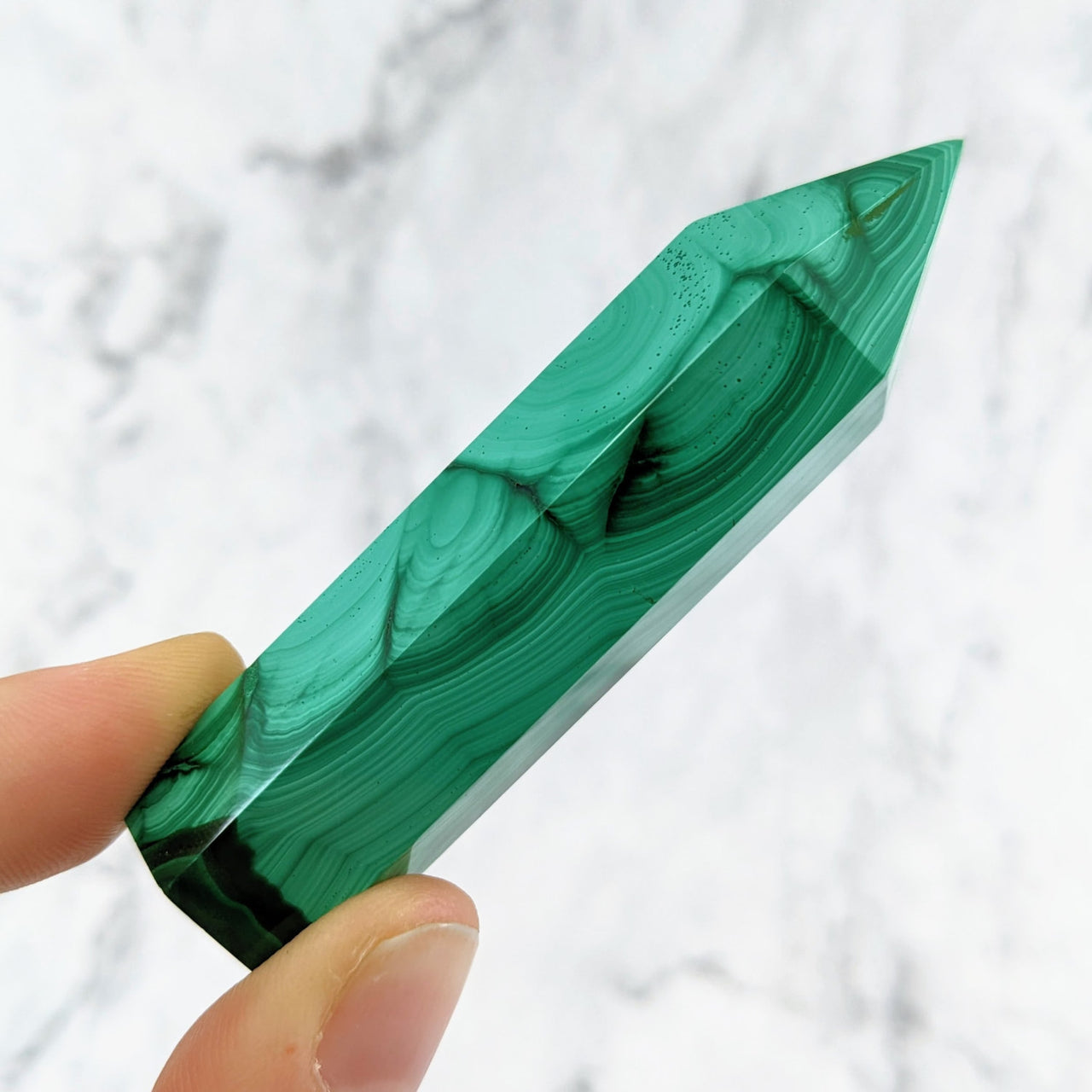 Hand holding a green malachite stone from the Malachite 2.7 - 3.1’ Tower #LV1460 product line