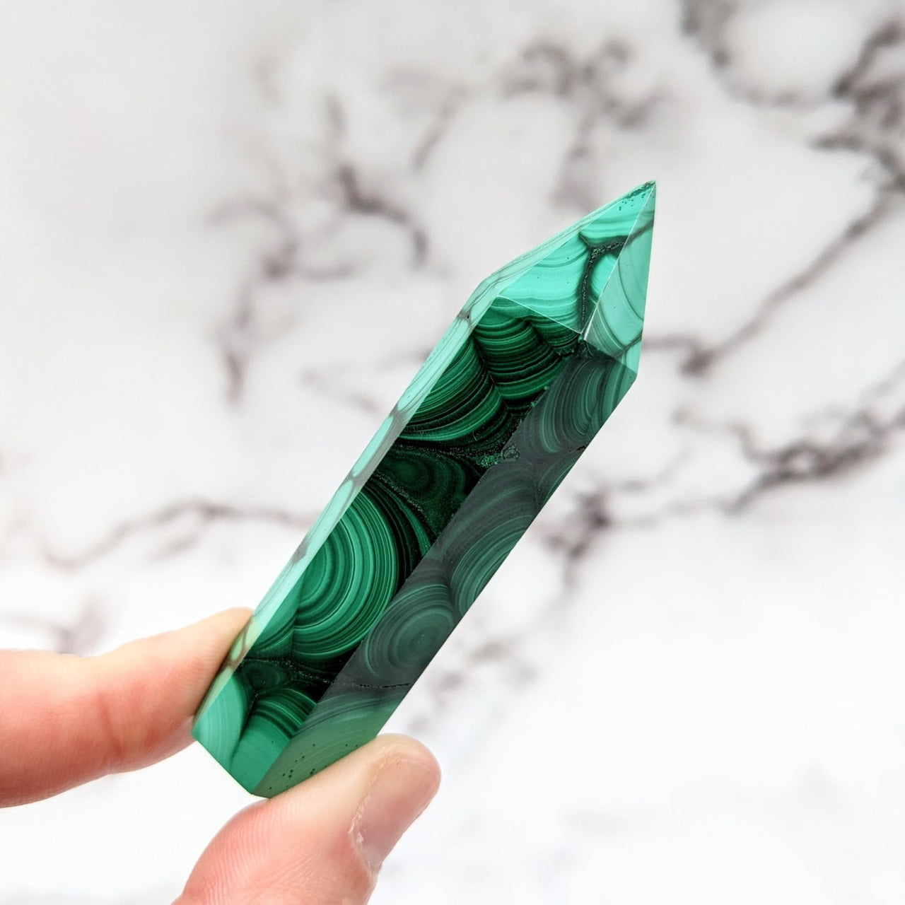 Hand holding a green marble pen from Malachite 2.7 - 3.1’ Tower #LV2570