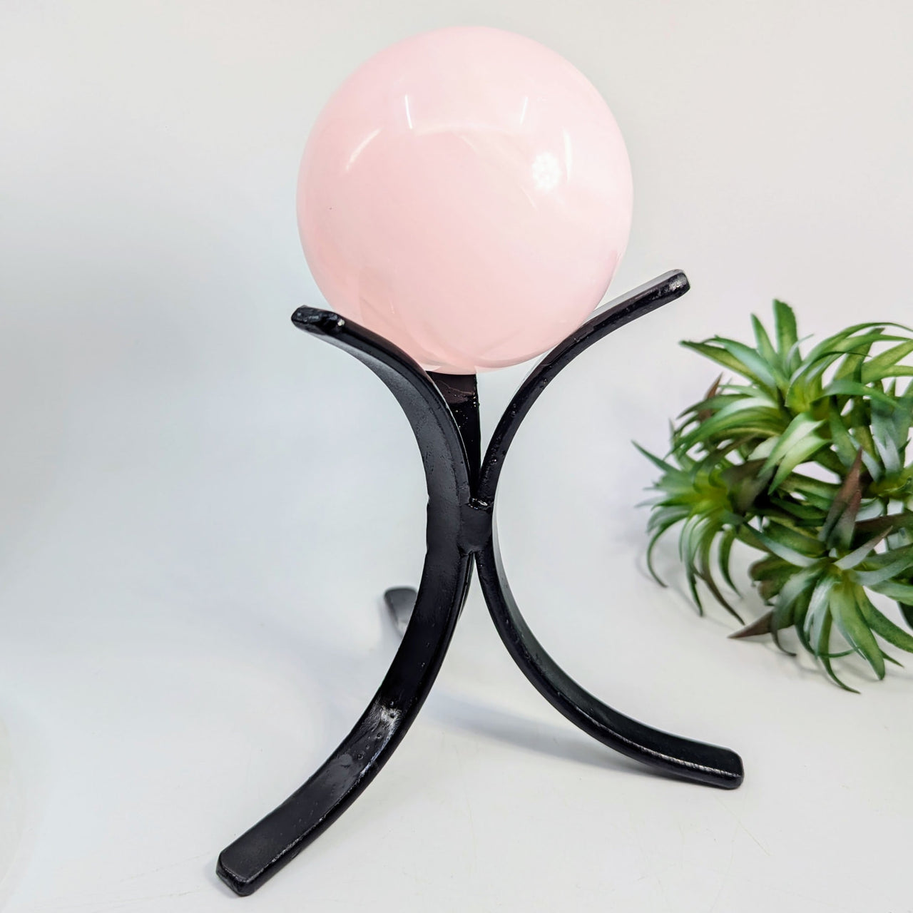 Pink crystal ball resting on a black metal stand for the Metal Sphere Stand 3 Prong 5 Tall