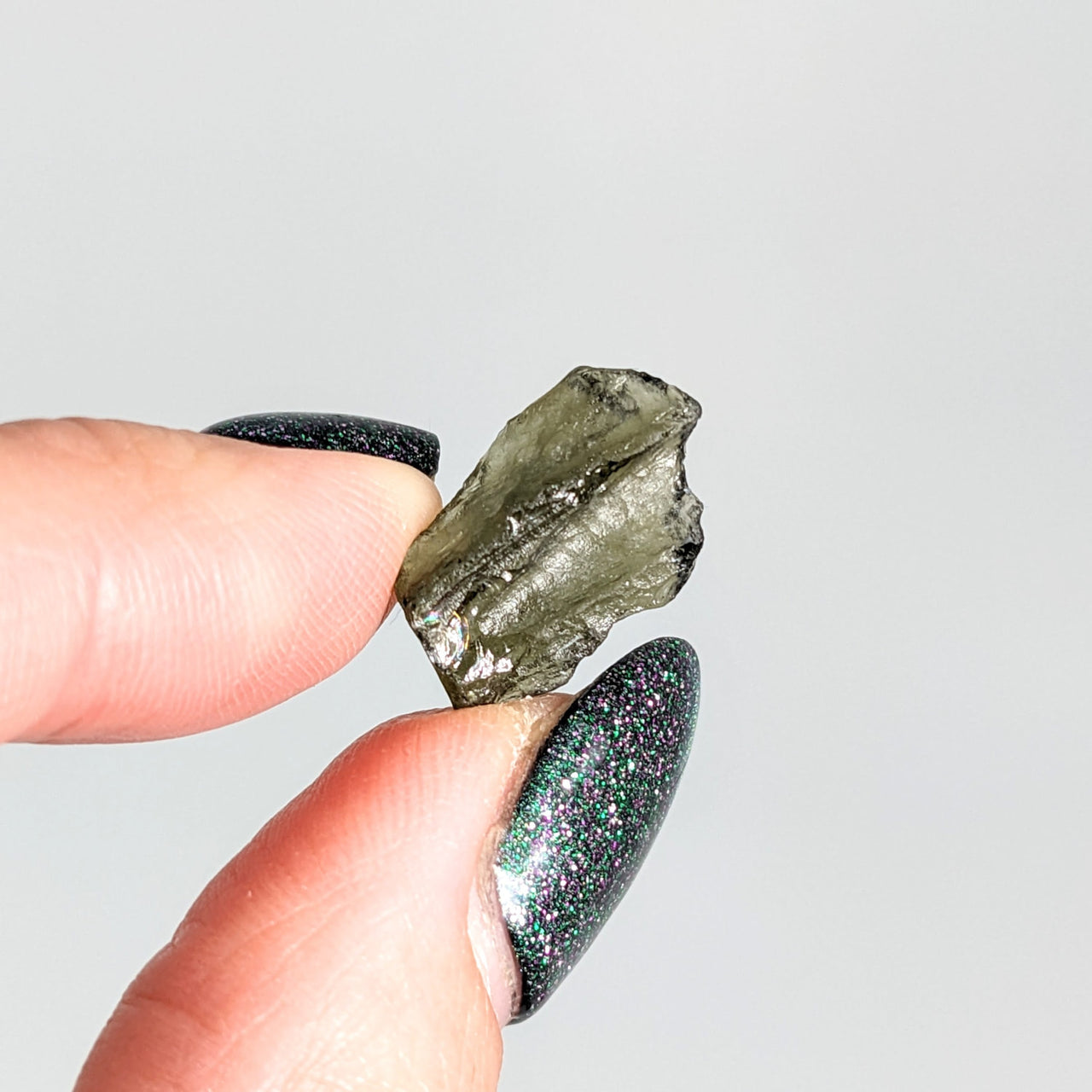 A person holding a green glittering piece of Moldavite 0.81g Rough Piece #SK9453