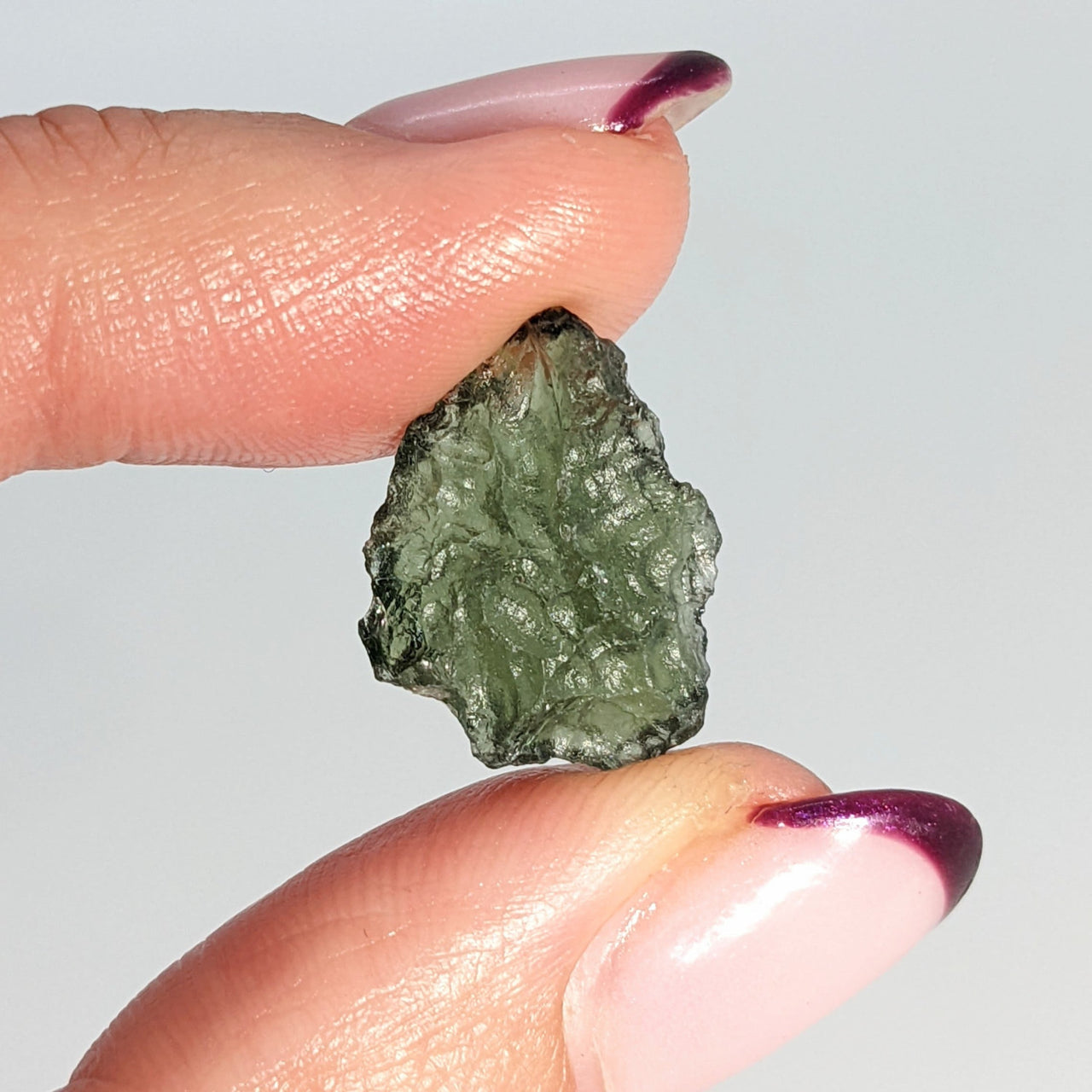 Woman holding rough cut moldavite crystal between fingers