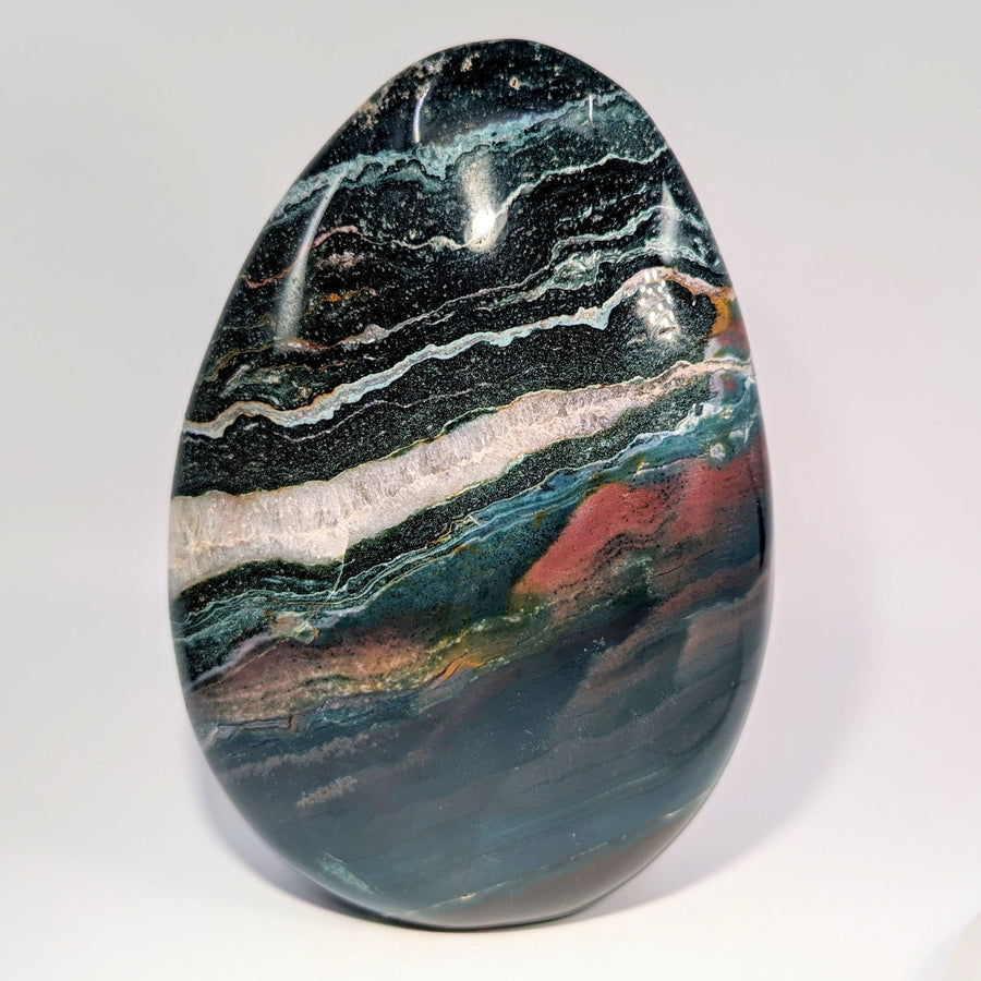 Polished 7-inch ocean jasper egg with green, black, white, red swirls