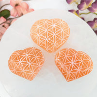 Peach-colored heart-shaped Selenite stones with Flower of Life etching for healing and decor