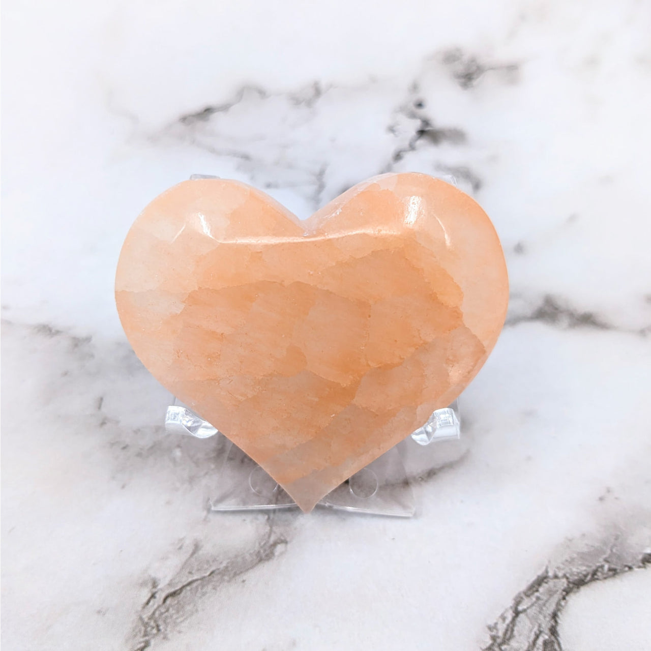 A heart-shaped Himalayan stone on a marble table, Peach Selenite 2.1’ Heart #LV4133