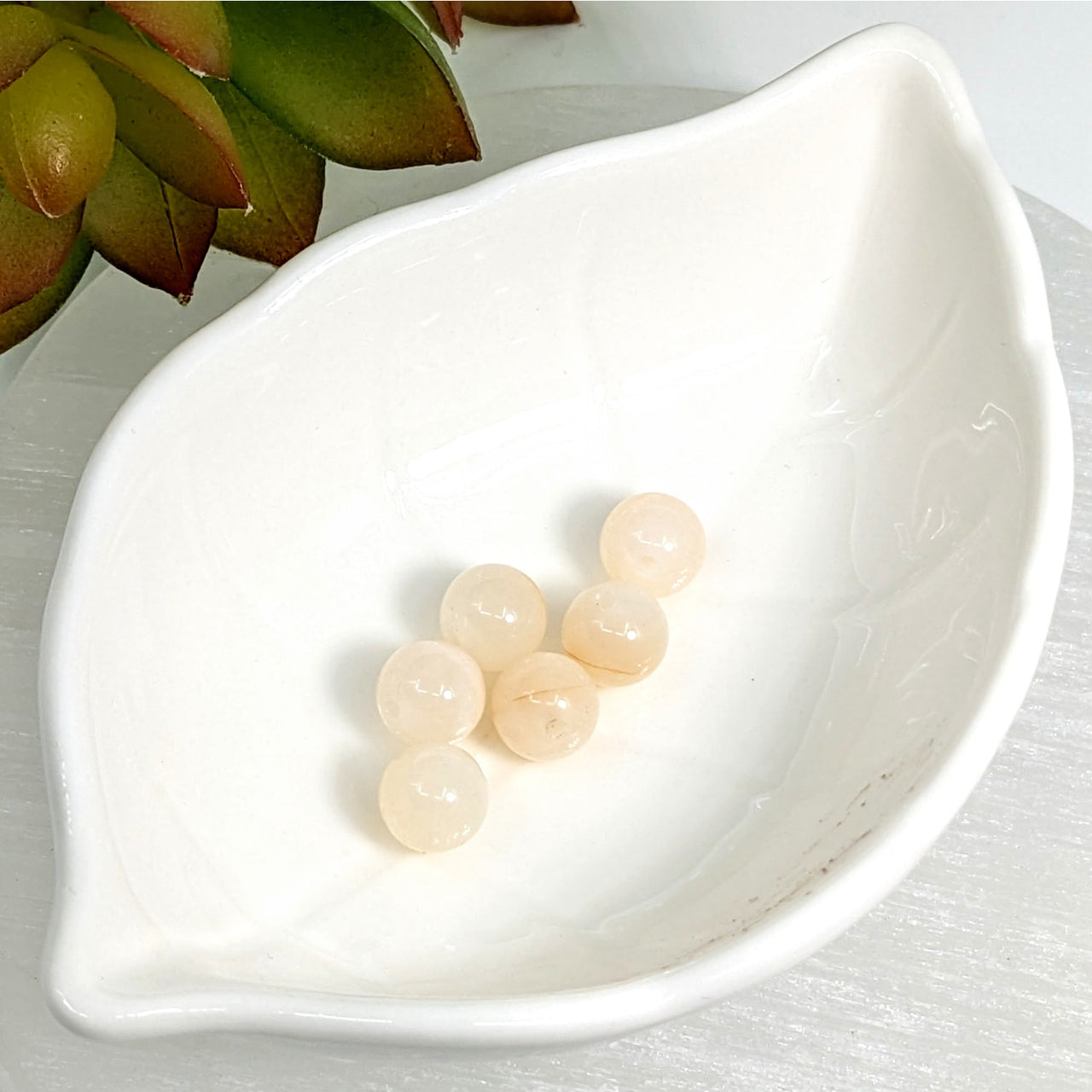 White leaf-shaped dish with Peach White Moonstone 8mm round beads displayed elegantly