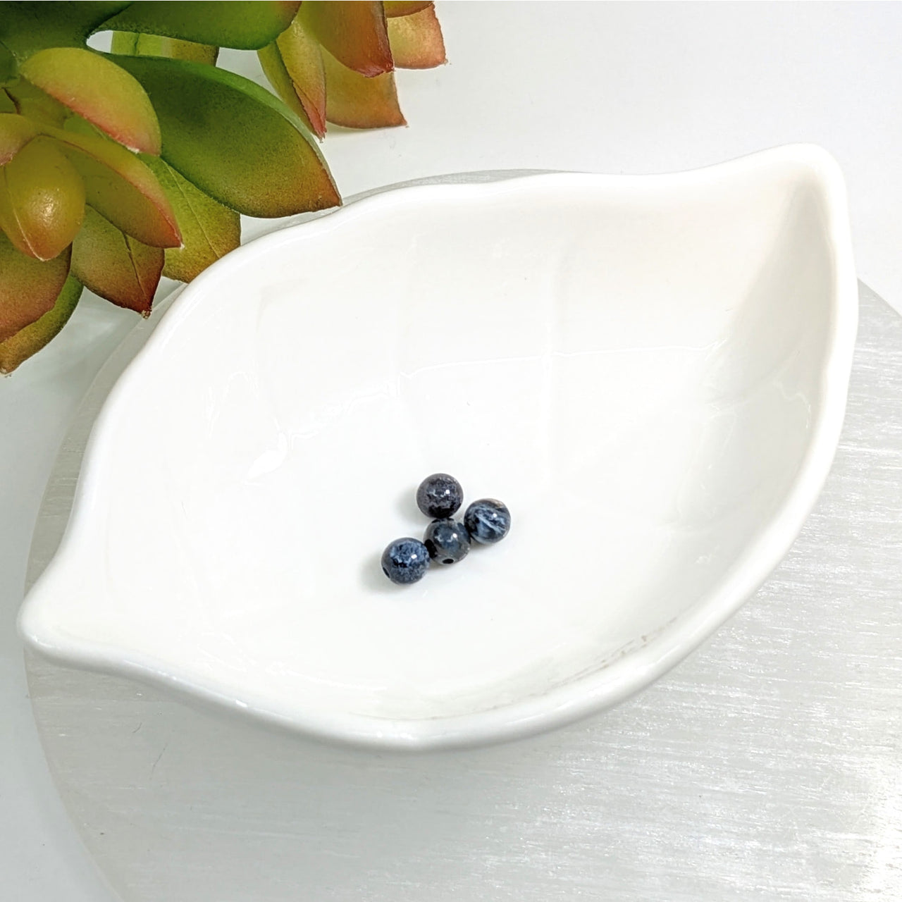 White leaf-shaped ceramic dish with three blueberries and Pietersite 5mm round beads