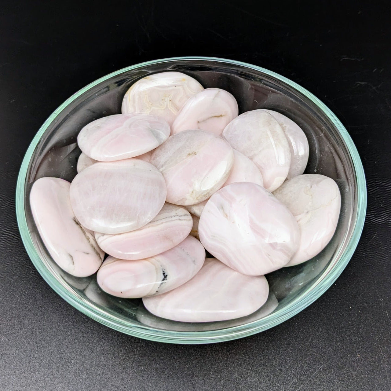 Bowl of Pink Mangano Calcite Palm Stones on Black Surface - Perfect for Healing Energy