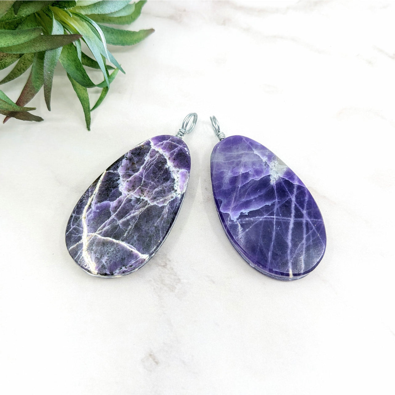 Two teardrop-shaped purple opal pendant stones with natural white veining attached to silver wire loops