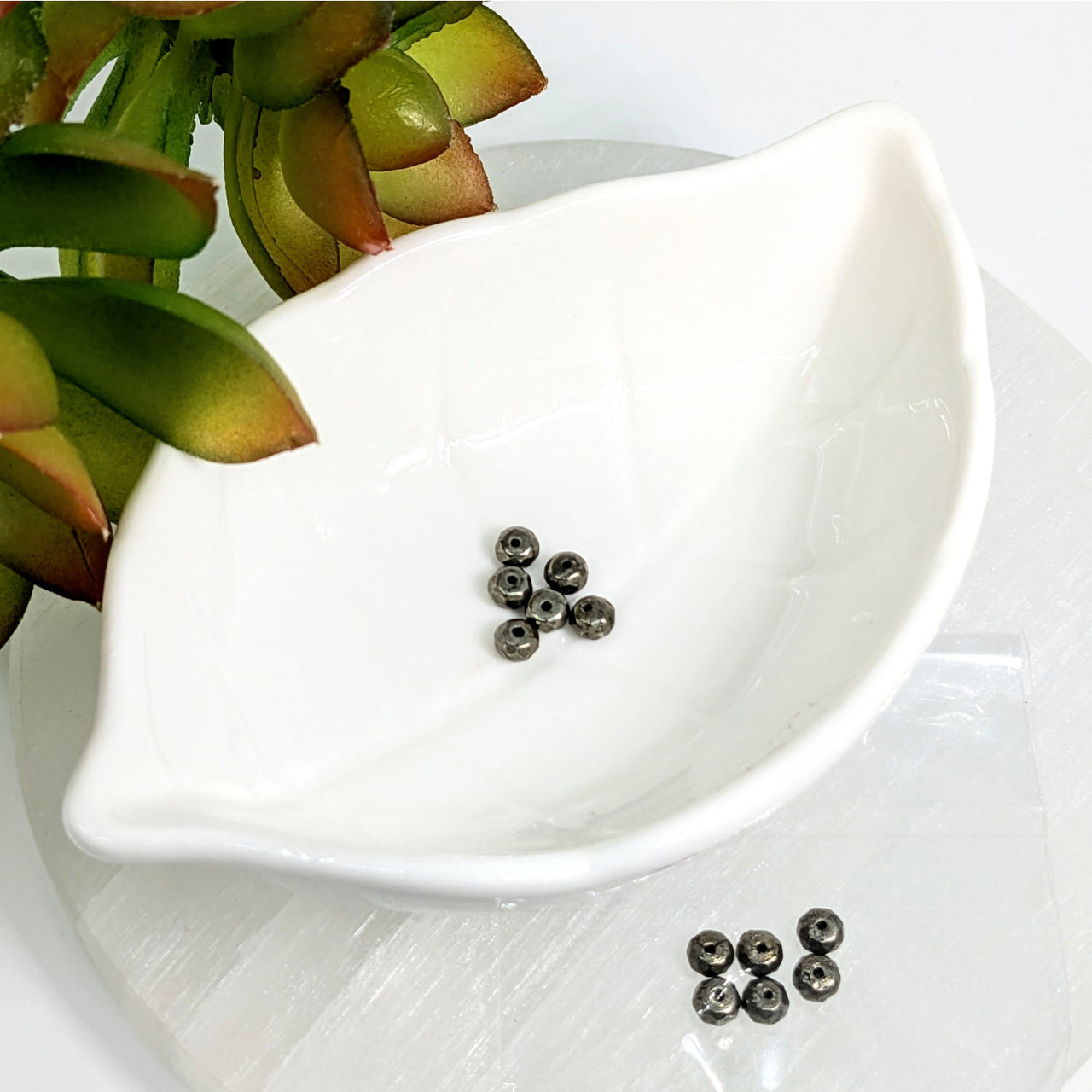 White leaf-shaped ceramic dish showcasing Pyrite 2mm Faceted Rondelle Beads