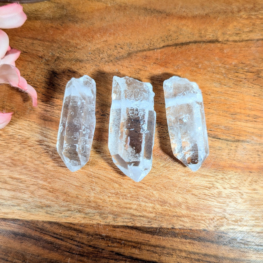 Three translucent clear quartz point crystals 1.2-1.5 inch drilled pendants for jewelry and gemstones on wood surface