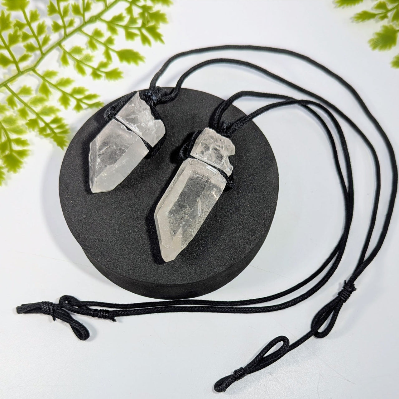 Two clear quartz crystal point pendants on black cord necklace displayed on dark base jewelry gemstones crystals