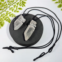 Two clear quartz crystal point pendants on black cord necklace displayed on dark base jewelry gemstones crystals