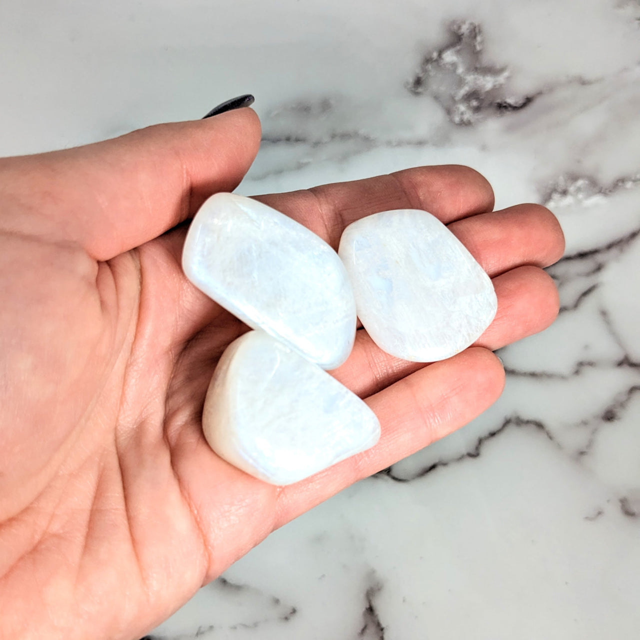 Hand holding two heart-shaped white sea glass tumbled stones from Rainbow Ice Moonstone