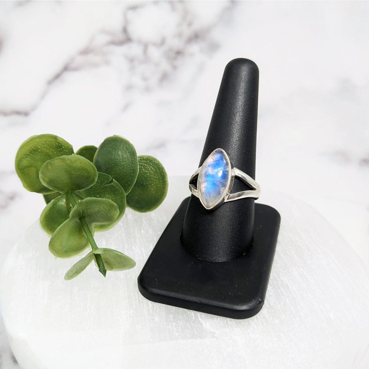 Beautiful Rainbow Moonstone S.S. Marquis Ring #LV3963 with a blue stone on a black stand