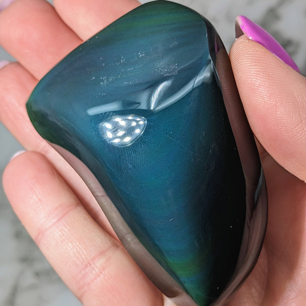 A person holding a large green and blue Rainbow Obsidian Freeform Pebble #LV5070