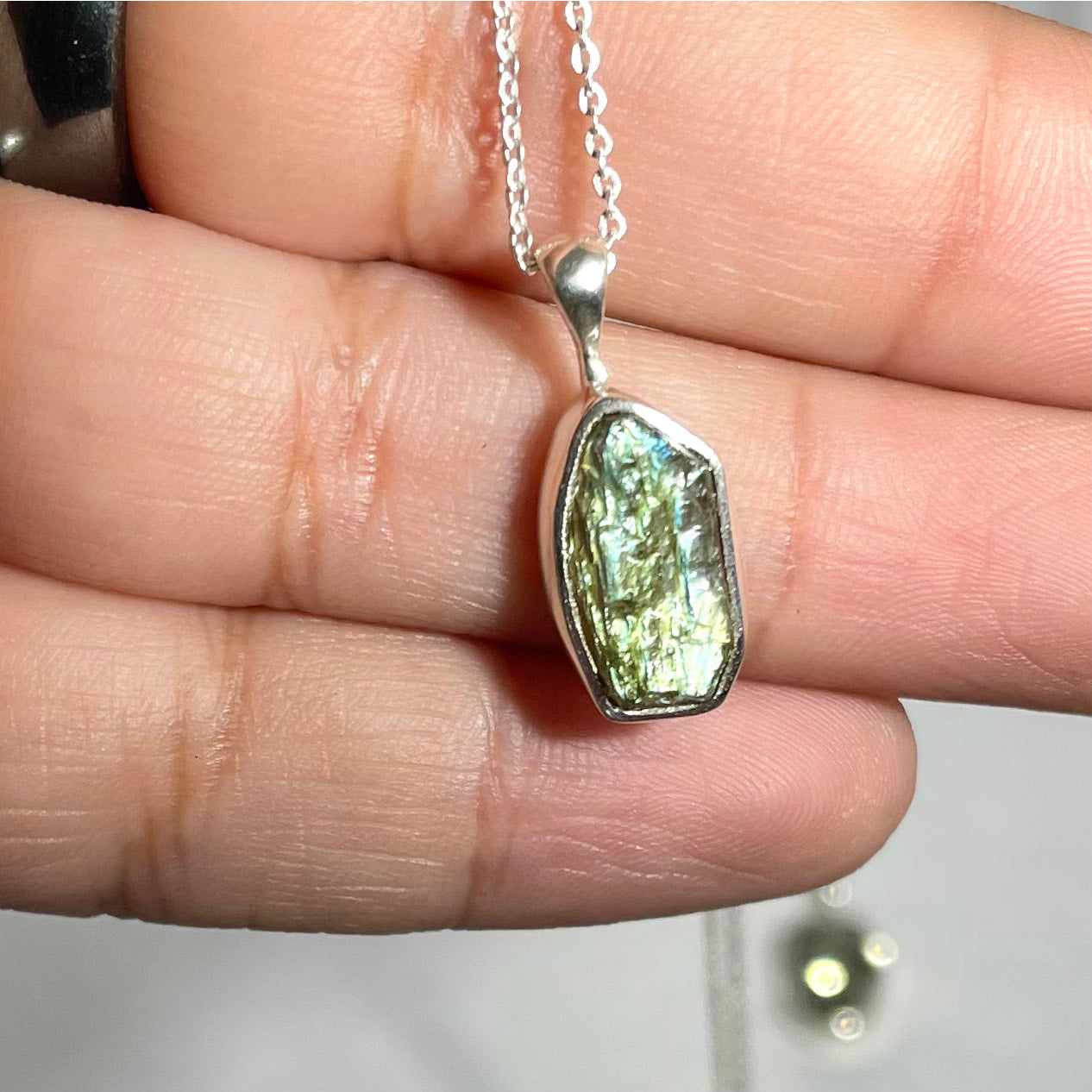 A person holding a green gems pendant for positive energy, Raw Sterling Silver Crystal Pendant